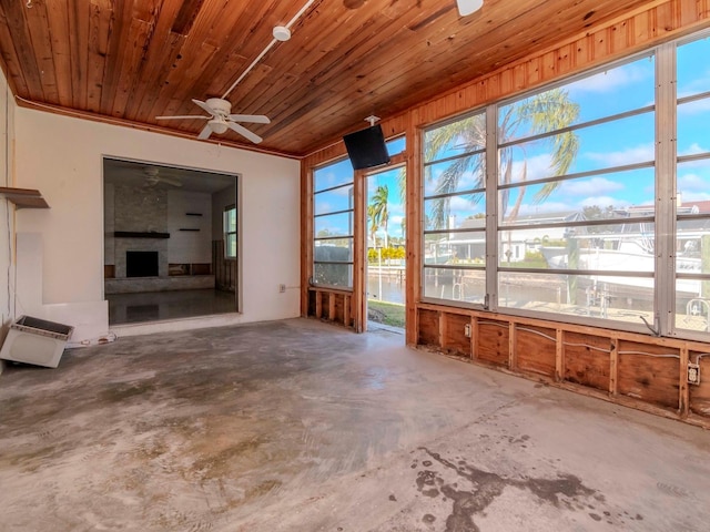 unfurnished sunroom with a large fireplace, ceiling fan, and wooden ceiling