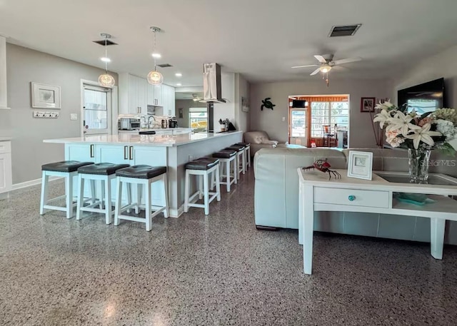 kitchen with a breakfast bar area, ceiling fan, decorative light fixtures, white cabinetry, and island exhaust hood