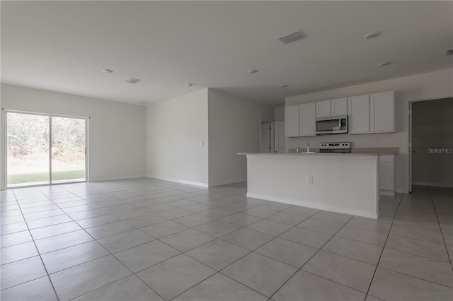 kitchen with appliances with stainless steel finishes, light tile patterned floors, a kitchen island with sink, and white cabinetry