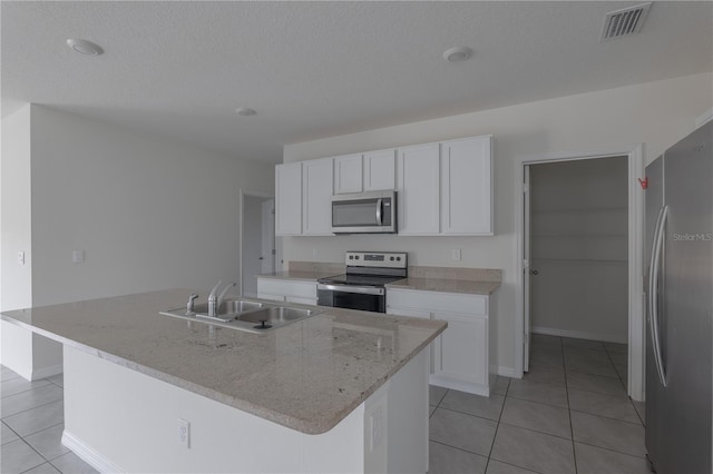 kitchen with stainless steel appliances, an island with sink, light tile patterned floors, sink, and white cabinetry