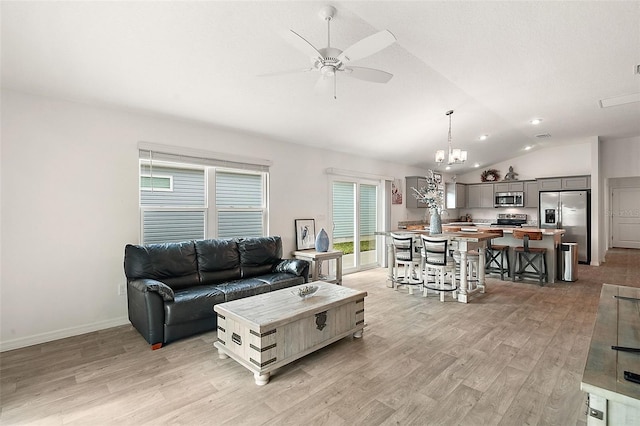 living room featuring ceiling fan with notable chandelier, light hardwood / wood-style floors, and vaulted ceiling