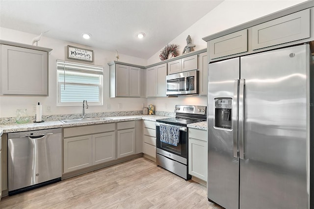 kitchen with appliances with stainless steel finishes, light stone counters, vaulted ceiling, sink, and light hardwood / wood-style floors