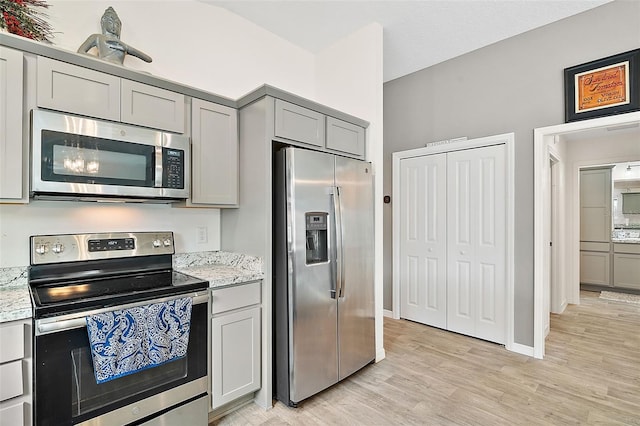 kitchen with gray cabinets, light stone countertops, light hardwood / wood-style flooring, and stainless steel appliances