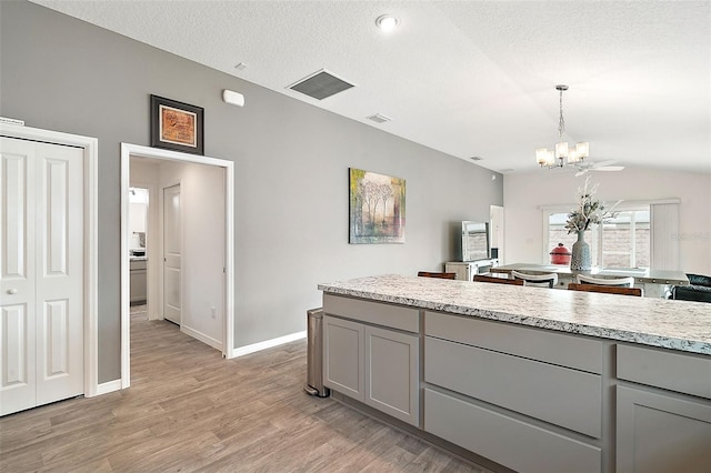 kitchen with a textured ceiling, pendant lighting, light hardwood / wood-style flooring, a notable chandelier, and gray cabinets