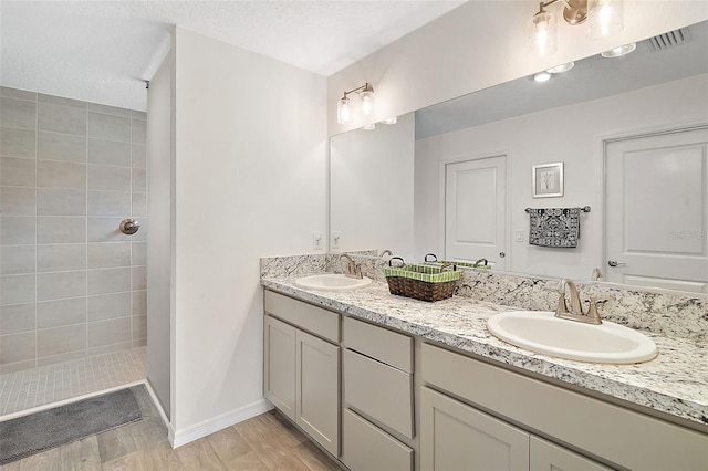 bathroom with a textured ceiling, vanity, and a tile shower