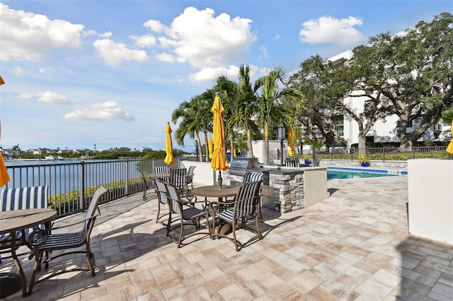 view of patio featuring an outdoor kitchen, a water view, area for grilling, a community pool, and a bar