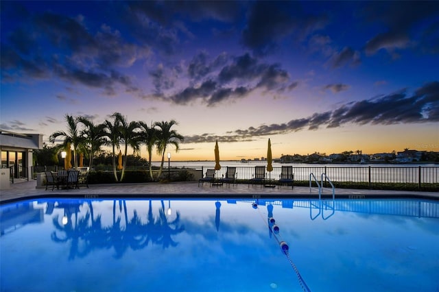 pool at dusk with a patio and a water view