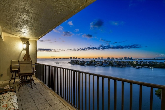 balcony at dusk featuring a water view