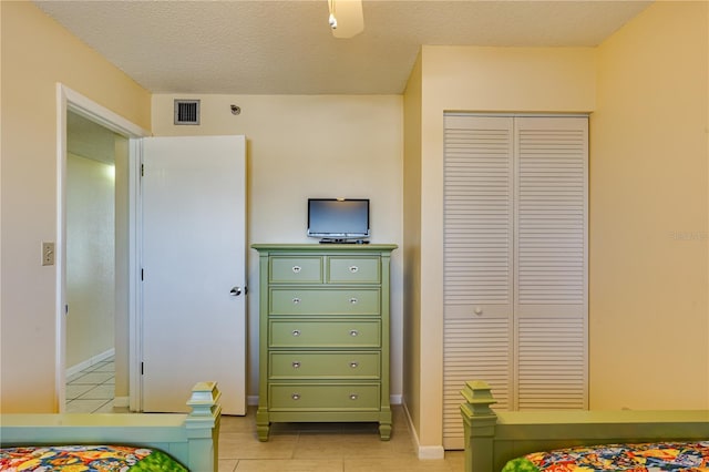 tiled bedroom with ceiling fan, a closet, and a textured ceiling