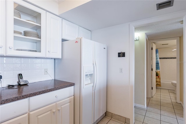 kitchen with decorative backsplash, white cabinetry, light tile patterned floors, and white refrigerator with ice dispenser