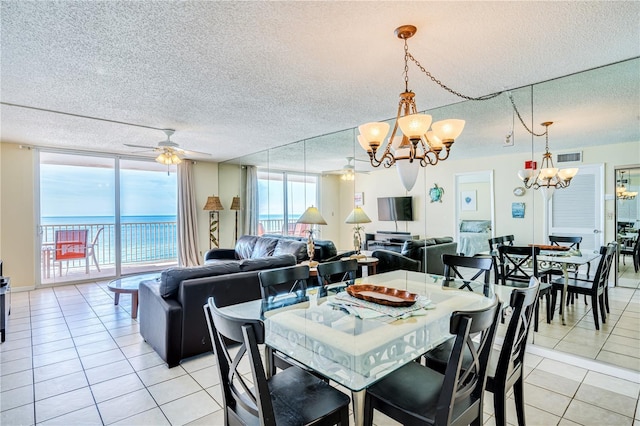 dining area featuring ceiling fan with notable chandelier, expansive windows, a water view, light tile patterned floors, and a textured ceiling