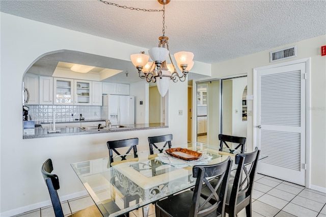 dining space featuring sink, light tile patterned flooring, a textured ceiling, and a notable chandelier