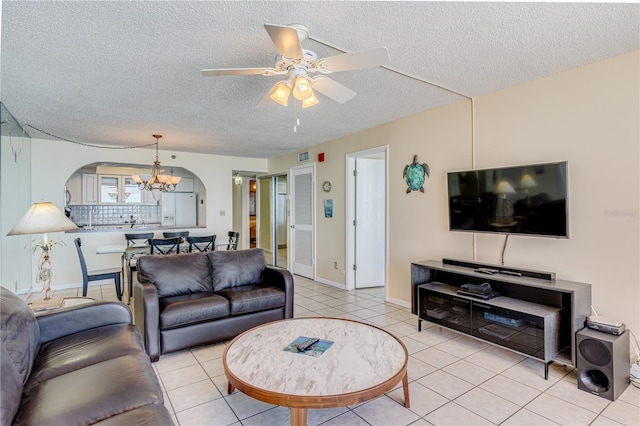 living room featuring light tile patterned floors, ceiling fan with notable chandelier, and a textured ceiling