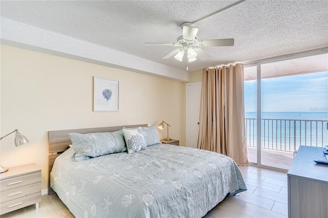 tiled bedroom with expansive windows, a textured ceiling, access to outside, ceiling fan, and a water view