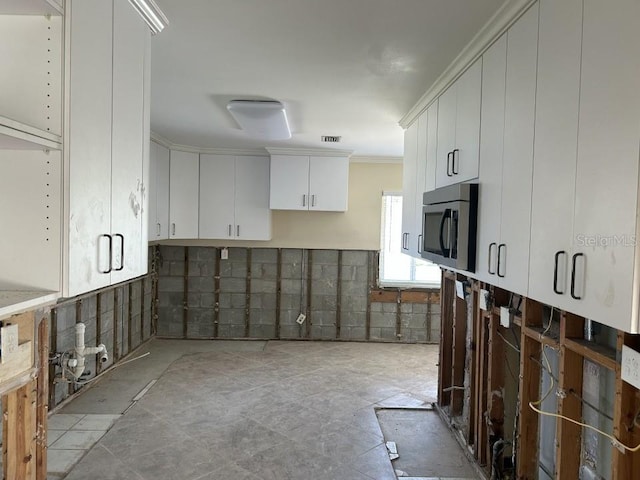 kitchen featuring white cabinets, stainless steel microwave, crown molding, and visible vents