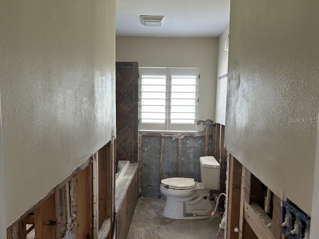 full bath featuring toilet, visible vents, and a textured wall