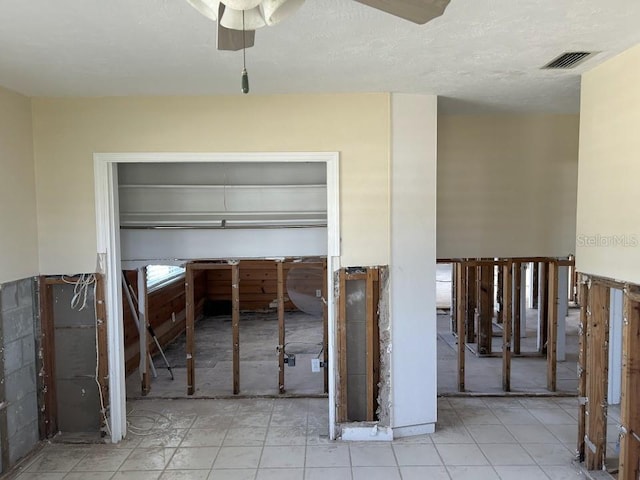 interior space with wainscoting, visible vents, ceiling fan, and a textured ceiling