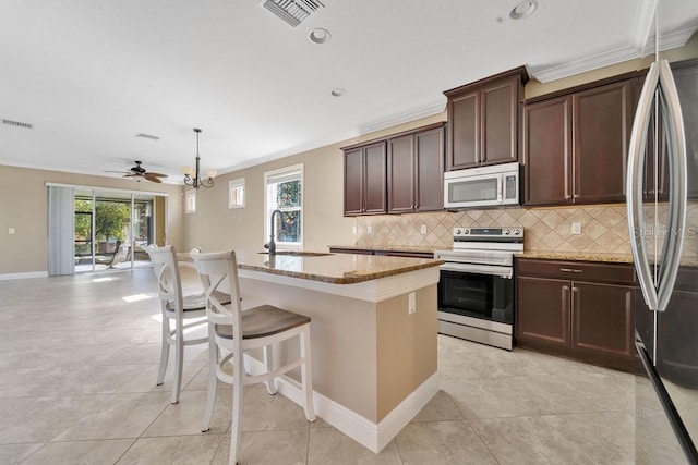 kitchen featuring light stone countertops, stainless steel appliances, crown molding, decorative light fixtures, and a kitchen island