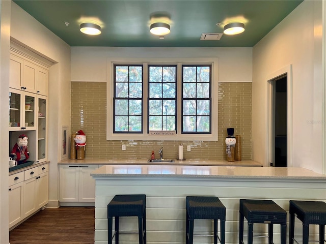 kitchen featuring a kitchen bar, light stone countertops, sink, white cabinets, and dark hardwood / wood-style floors