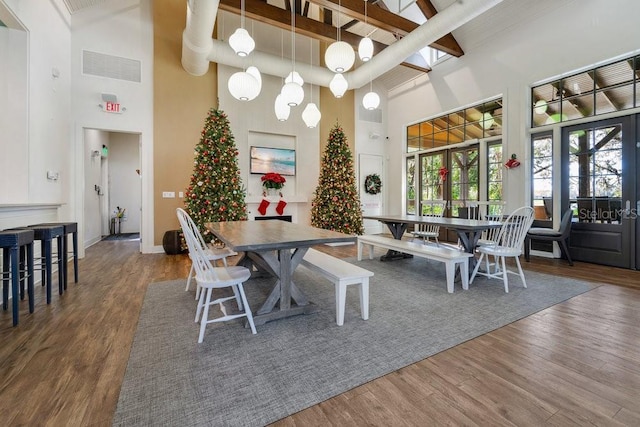 dining room featuring hardwood / wood-style floors, a towering ceiling, french doors, and beam ceiling