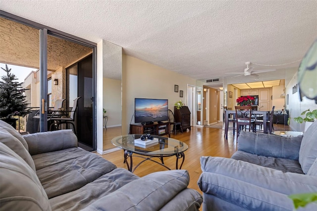 living room featuring ceiling fan, light wood-type flooring, and a textured ceiling