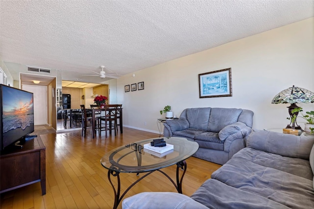 living room with ceiling fan, a textured ceiling, and hardwood / wood-style flooring