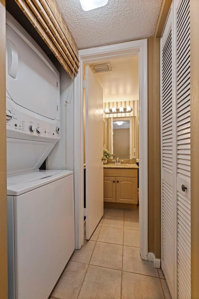 clothes washing area with a textured ceiling, sink, light tile patterned floors, and stacked washer / dryer