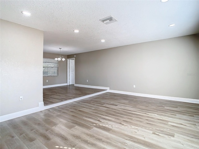 empty room featuring a notable chandelier, light wood-type flooring, and a textured ceiling