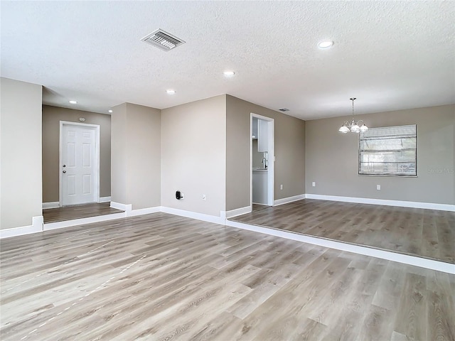 spare room featuring a chandelier, light hardwood / wood-style floors, and a textured ceiling