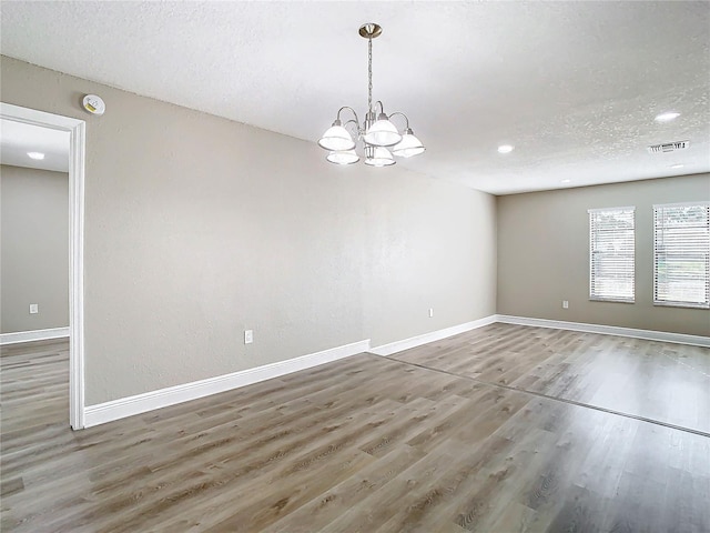 unfurnished room featuring hardwood / wood-style floors, a textured ceiling, and an inviting chandelier