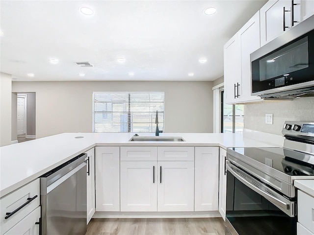 kitchen with kitchen peninsula, stainless steel appliances, sink, light hardwood / wood-style floors, and white cabinetry