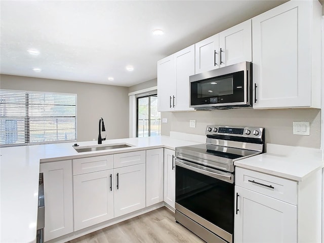 kitchen featuring sink, stainless steel appliances, kitchen peninsula, white cabinets, and light wood-type flooring