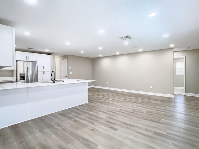 kitchen with stainless steel refrigerator with ice dispenser, light wood-type flooring, white cabinetry, and sink