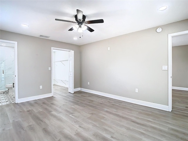 unfurnished bedroom with a walk in closet, connected bathroom, light hardwood / wood-style floors, and ceiling fan