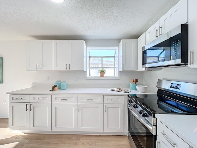 kitchen featuring a textured ceiling, stainless steel appliances, white cabinetry, and light hardwood / wood-style floors