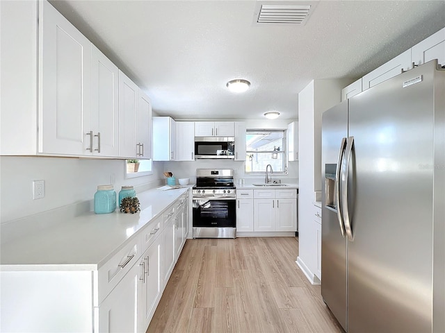 kitchen featuring appliances with stainless steel finishes, a textured ceiling, sink, light hardwood / wood-style flooring, and white cabinetry