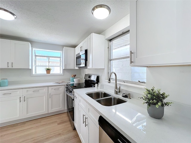 kitchen featuring sink, a textured ceiling, light hardwood / wood-style floors, white cabinetry, and stainless steel appliances