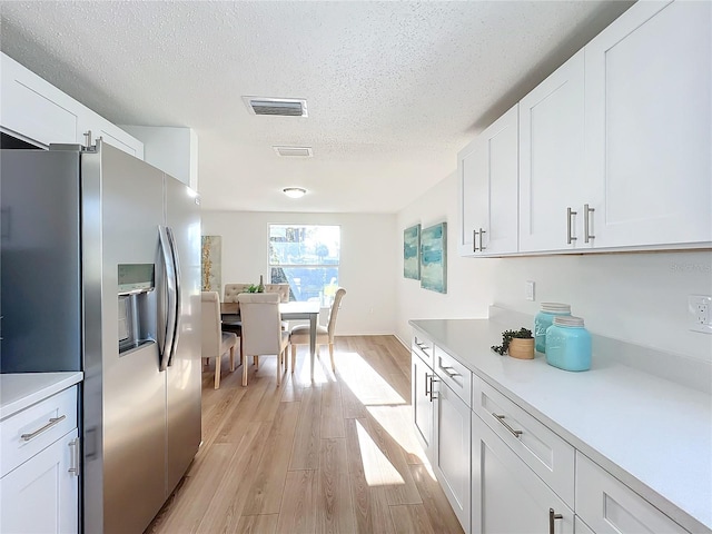 kitchen featuring white cabinets, stainless steel fridge, a textured ceiling, and light hardwood / wood-style flooring