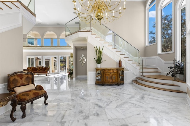 foyer entrance featuring a decorative wall, a towering ceiling, marble finish floor, ornamental molding, and stairway