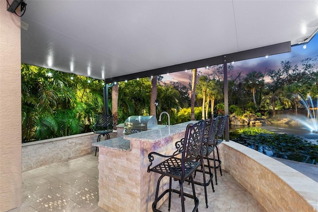 patio terrace at dusk with outdoor wet bar, grilling area, and an outdoor kitchen