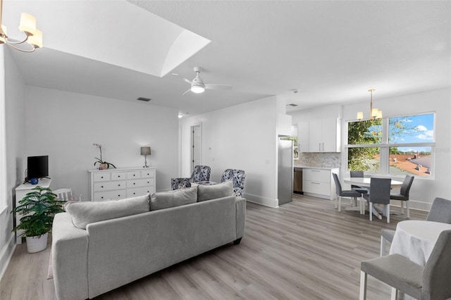 living room with visible vents, light wood-style flooring, baseboards, and ceiling fan with notable chandelier