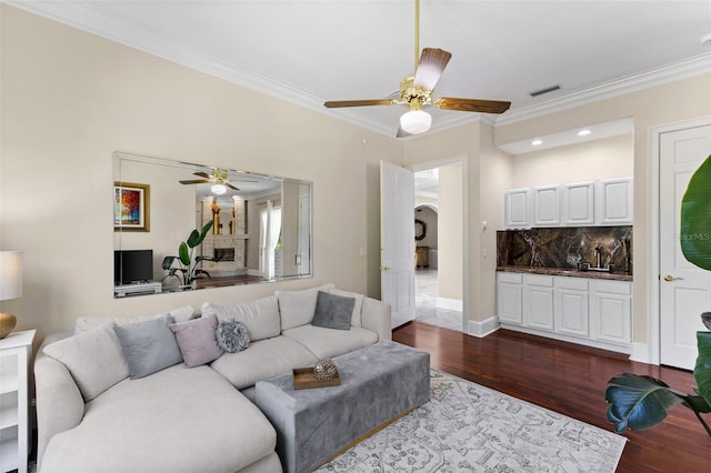 living area featuring visible vents, a fireplace with raised hearth, dark wood-style floors, ceiling fan, and ornamental molding