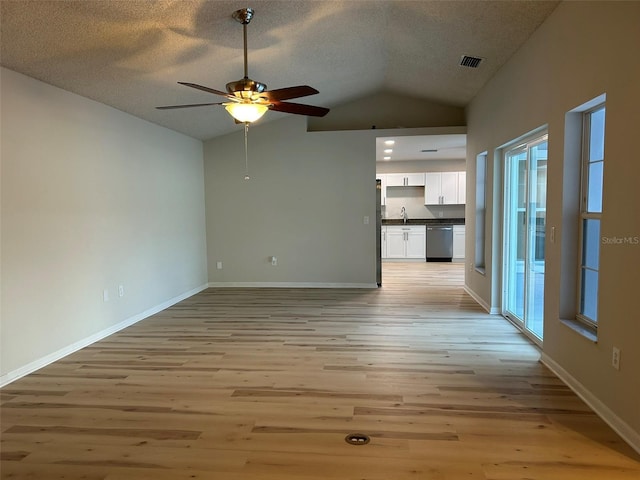 unfurnished living room featuring light wood-type flooring, baseboards, a textured ceiling, and vaulted ceiling