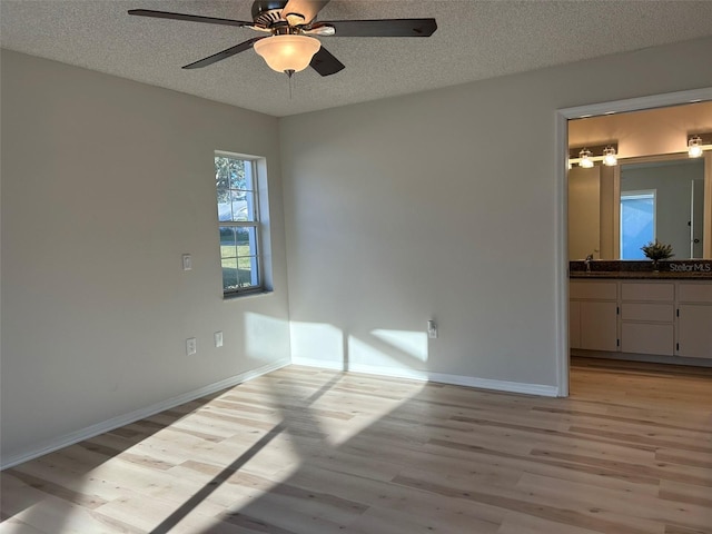 unfurnished bedroom featuring baseboards, a textured ceiling, light wood-style floors, and a sink