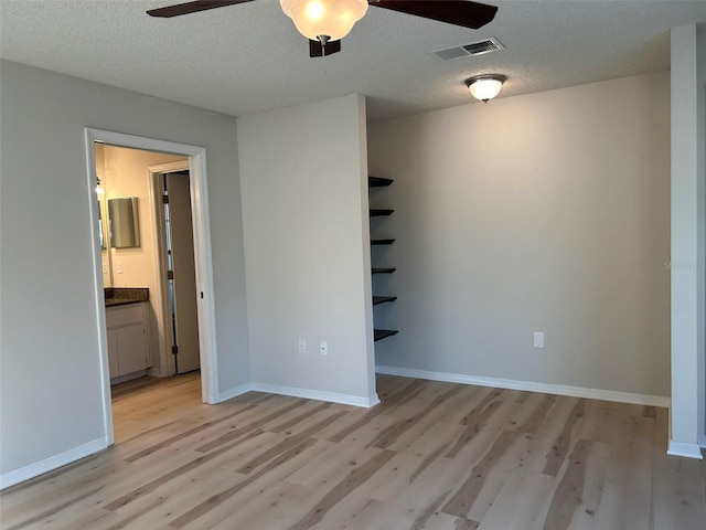 spare room with visible vents, baseboards, ceiling fan, light wood-type flooring, and a textured ceiling