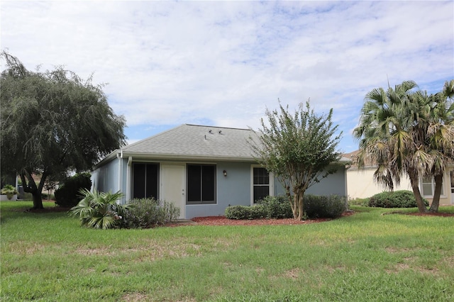 view of front of home with stucco siding, a front yard, and a shingled roof