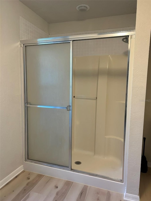 full bathroom featuring baseboards, a stall shower, and wood finished floors