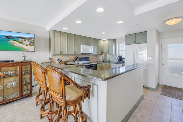 kitchen with kitchen peninsula, tasteful backsplash, white appliances, sink, and dark stone countertops