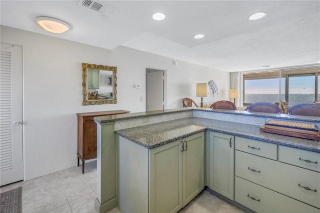 kitchen featuring kitchen peninsula, dark stone countertops, light tile patterned flooring, and green cabinetry