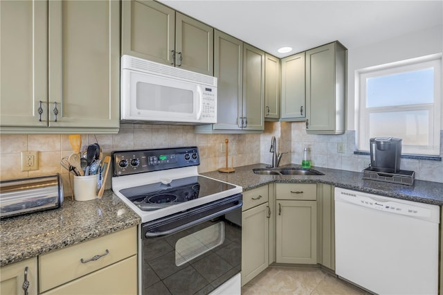 kitchen featuring tasteful backsplash, dark stone counters, white appliances, sink, and light tile patterned floors